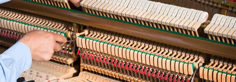 Piano technician repairing an upright piano action mechanism